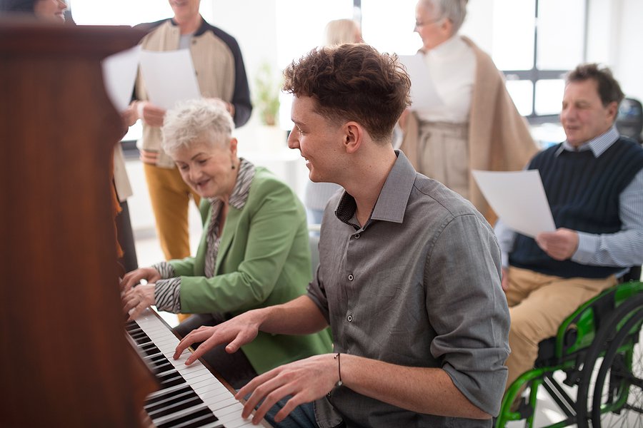 Senior Woman With Young Teacher Playing At Piano In Choir Rehear